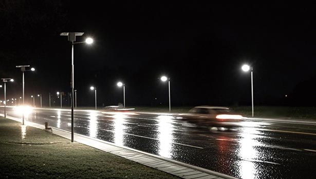 Solar street lights lighting up a wet road at night with vehicles passing by