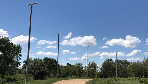 Solar street lights lining a countryside path, with clear blue sky and scattered clouds