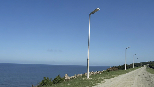 Solar street lights installed along a coastal dirt road under a clear blue sky