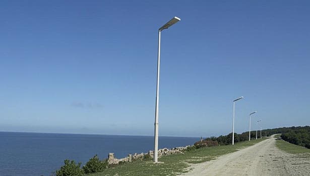 Solar street lights installed along coastal roadside under clear blue sky