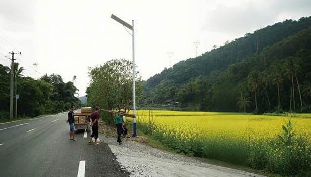 Workers installing a solar street light by a rural road with yellow crops and hills