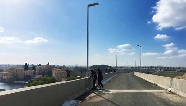 Solar street lights installed on a bridge, with pedestrians and a scenic background, highlighting urban application