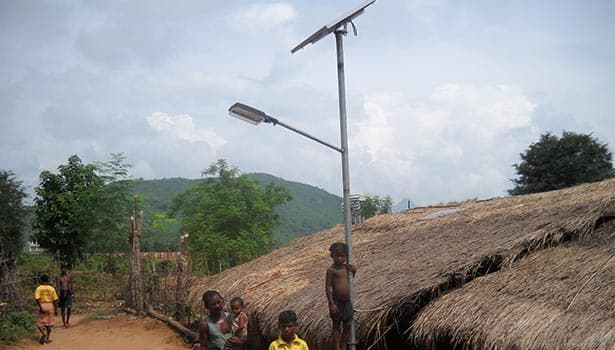 Solar LED street light installed in a rural village, illuminating the area around thatched houses with villagers nearby
