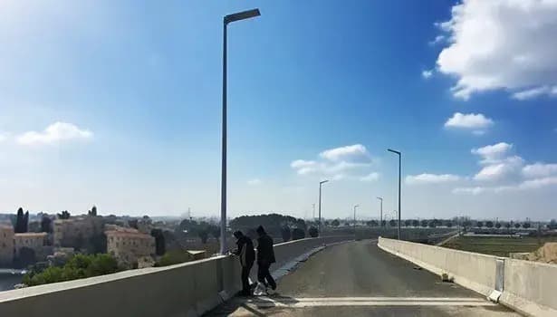 Two people walking beside solar street lights installed on a road bridge under a clear blue sky