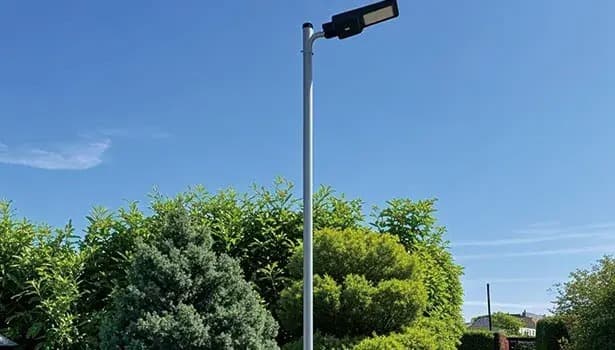 Solar-powered street light pole standing among lush green bushes under a bright blue sky