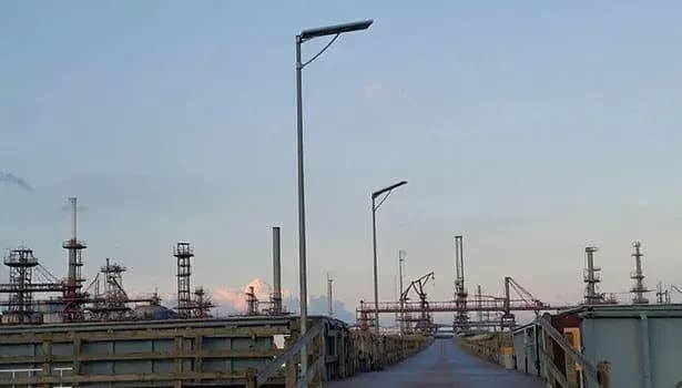 Solar street lights installed along a pathway in an industrial zone with refinery structures during dusk