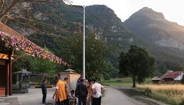 Solar street light in a rural village setting with mountains and people gathered nearby