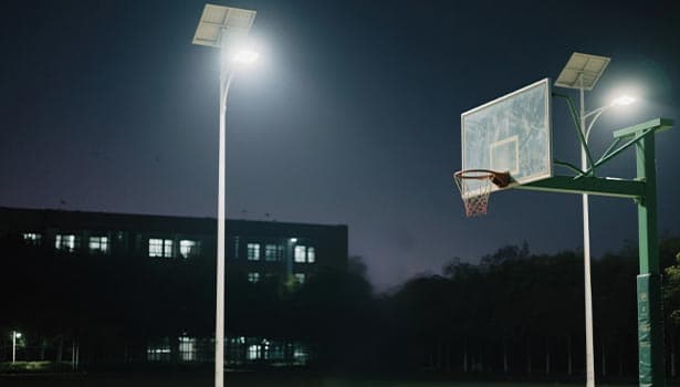 Solar street lights brightening a basketball court as part of a sports facility construction project at night.