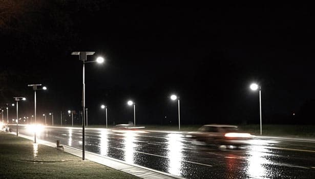 Solar street lights brightly illuminating a wet road at night, ensuring visibility and traffic safety.