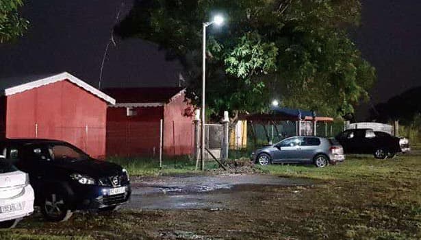 Solar street light illuminating outdoor site at night, enhancing security and visibility around buildings and parked cars.